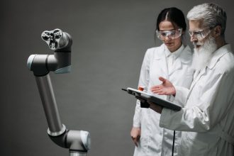 Pesquisadores de jaleco e óculos de proteção trabalham com um braço robótico em um laboratório.