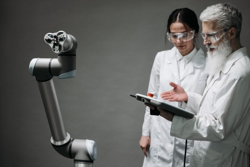 Pesquisadores de jaleco e óculos de proteção trabalham com um braço robótico em um laboratório.