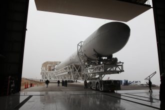 Booster de foguete recém-instalado sobre uma plataforma de transporte, sendo levado para um edifício de montagem em um centro espacial.