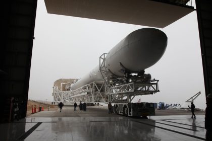 Booster de foguete recém-instalado sobre uma plataforma de transporte, sendo levado para um edifício de montagem em um centro espacial.