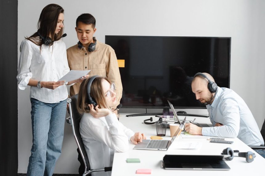 Equipe diversa de profissionais colaborando em um escritório moderno, com laptops e fones de ouvido.